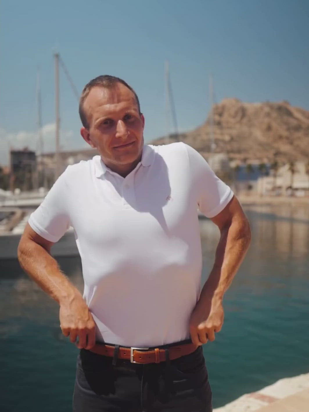 Iconic pánské polo triko z biobavlny bílé muž v přístavu u moře si upravuje kalhoty