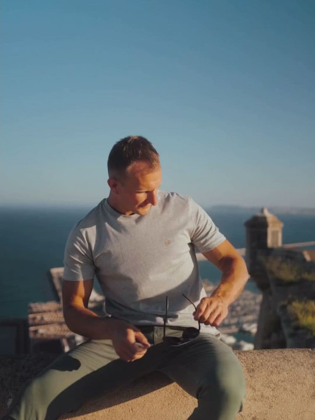Feel pánské tričko z biobavlny s kulatým výstřihem šedé žíhané muž sedí na zábradlí nad městem u moře