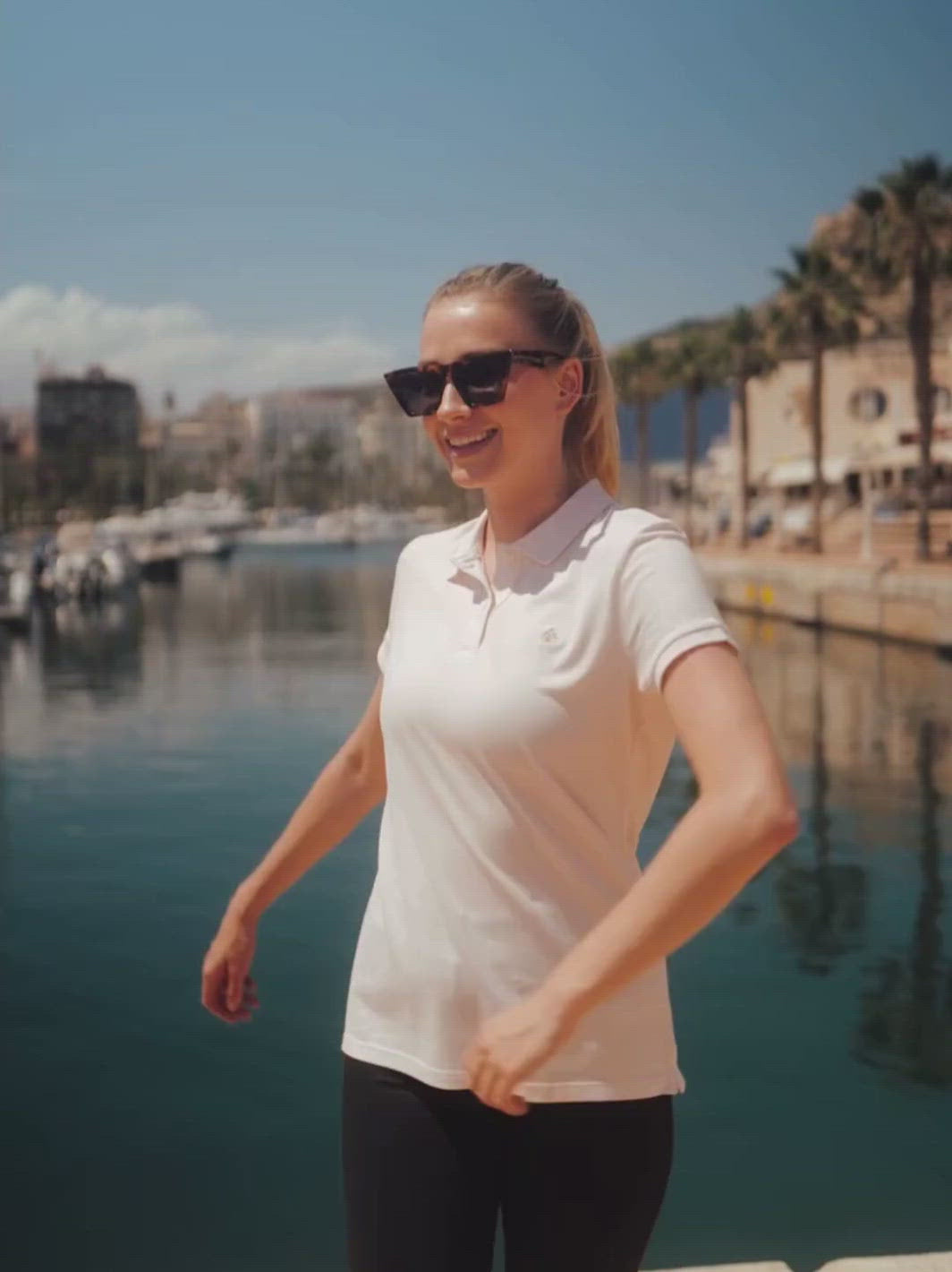 Milano dámské polo tričko z biobavlny růžové žena se otáčí v přístavu u moře s palmami a modrým nebem