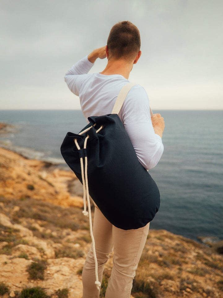 Marine plátěná taška z biobavlny námořní modrá muž stojí na útesu s taškou přes rameno a kouká na moře