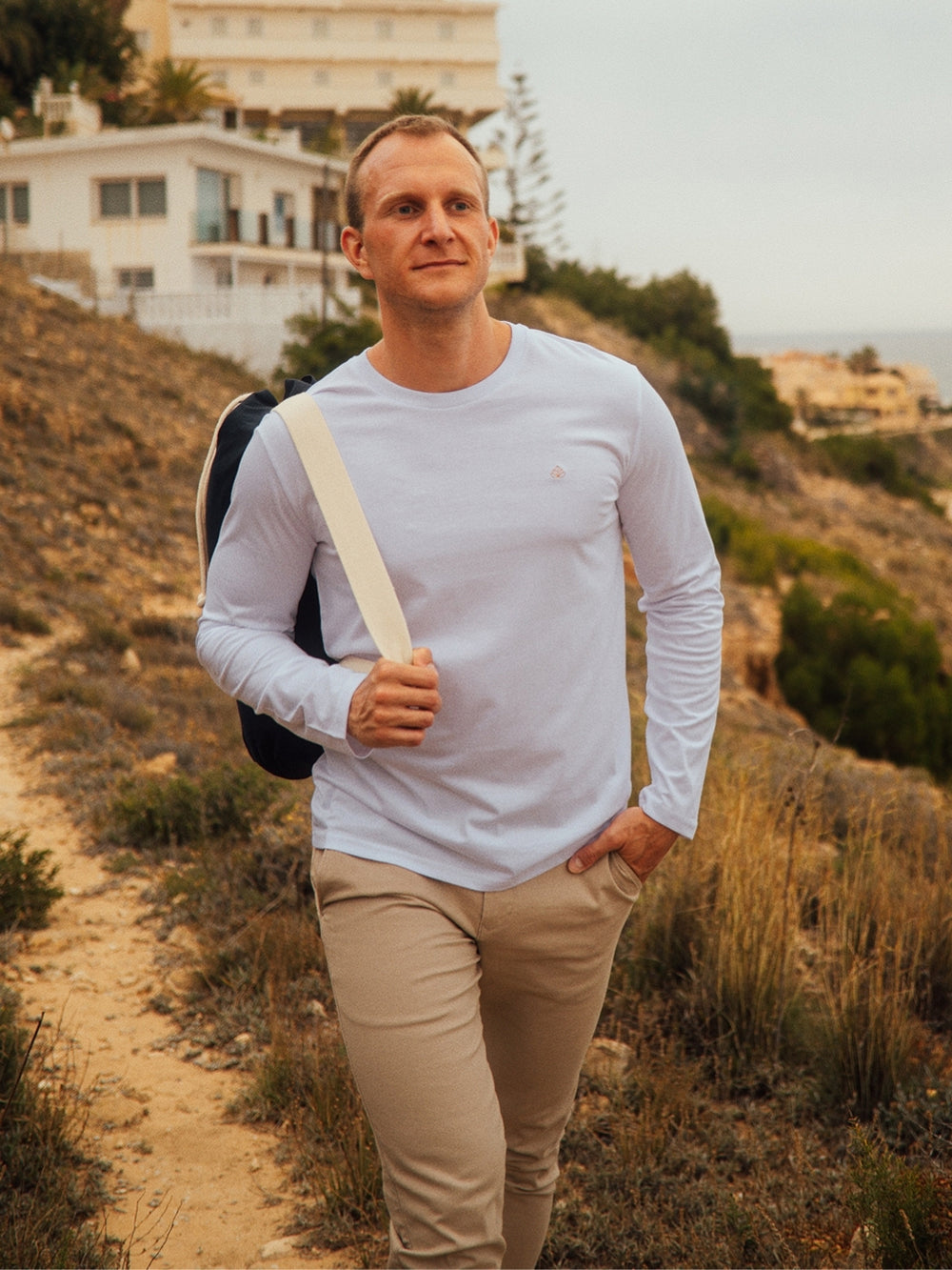 Teide pánské tričko s dlouhým rukávem z biobavlny s kulatým výstřihem bílé muž jde po útesu s taškou přes rameno